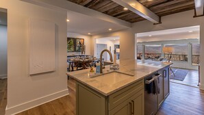 A spacious kitchen with a large island, wooden ceiling beams, and a view of the mountains through the balcony. - Hawthorn House at Hound Ears - STUNNING Grandfather views! Pool table! Updated! (Boone)