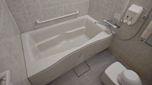 A bathroom with a bathtub, a toilet, and a handrail.