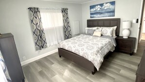 Un dormitorio con cama, mesitas de noche, lámpara, un cuadro y cortinas.