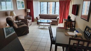 A living room with a sofa, armchair, coffee table, and dining table. - Palace 510 (Myrtle Beach)