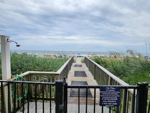 A wooden boardwalk leading to a beach with a sign indicating authorized access for residents and guests only, wristbands required, and a security contact number.