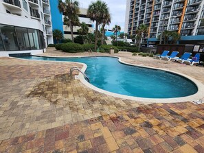A swimming pool with a brick deck, surrounded by palm trees and a multi-story building with balconies. - Palace 510 (Myrtle Beach)