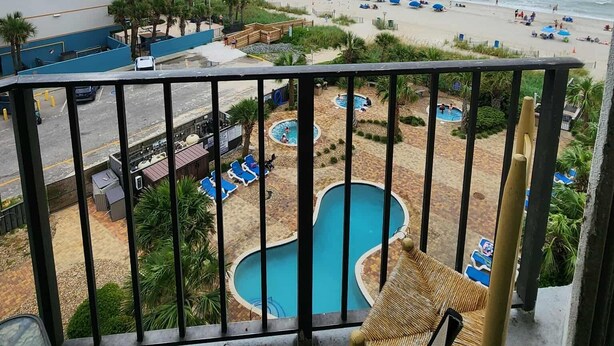 A balcony with a view of a beach, pool area, and a building. - Palace 510 (Myrtle Beach)
