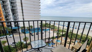 A balcony with a view of a beach, a pool area, and a parking lot. - Palace 510 (Myrtle Beach)