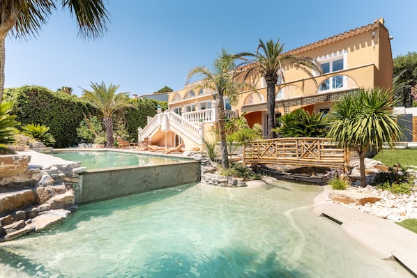A resort with a swimming pool, palm trees, and a wooden bridge. - Villa Halo, Lagoon Pool & Exclusive seaside getaway (Agde)