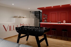 A modern kitchen with a foosball table, a red accent wall, and a bar area with stools. - Villa Halo, Lagoon Pool & Exclusive seaside getaway (Agde)