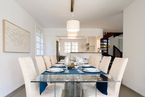 A dining area with a glass table, white chairs, and a chandelier. - Villa Halo, Lagoon Pool & Exclusive seaside getaway (Agde)
