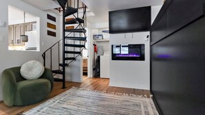 A modern living room with a green sofa, a patterned rug, a black staircase, and a flat-screen TV mounted on the wall. - Modern Mountain Apartment Unit 2 near Durango, CO. (Durango)