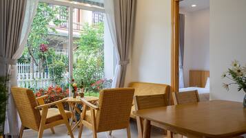 Een kamer met een houten tafel en stoelen, een raam met gordijnen en uitzicht op een tuin.