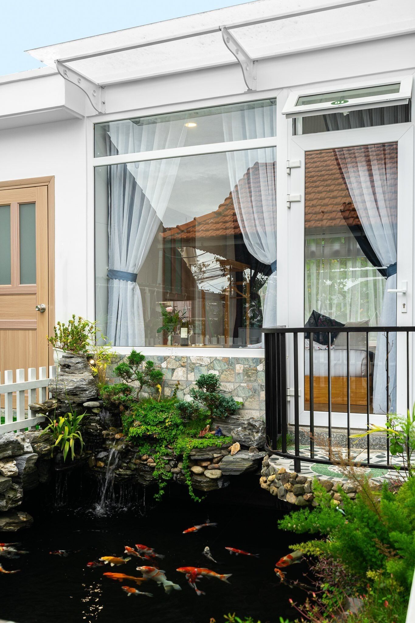 Een modern huis met een vijver met koi karpers, een klein watervalletje en een witte schutting.