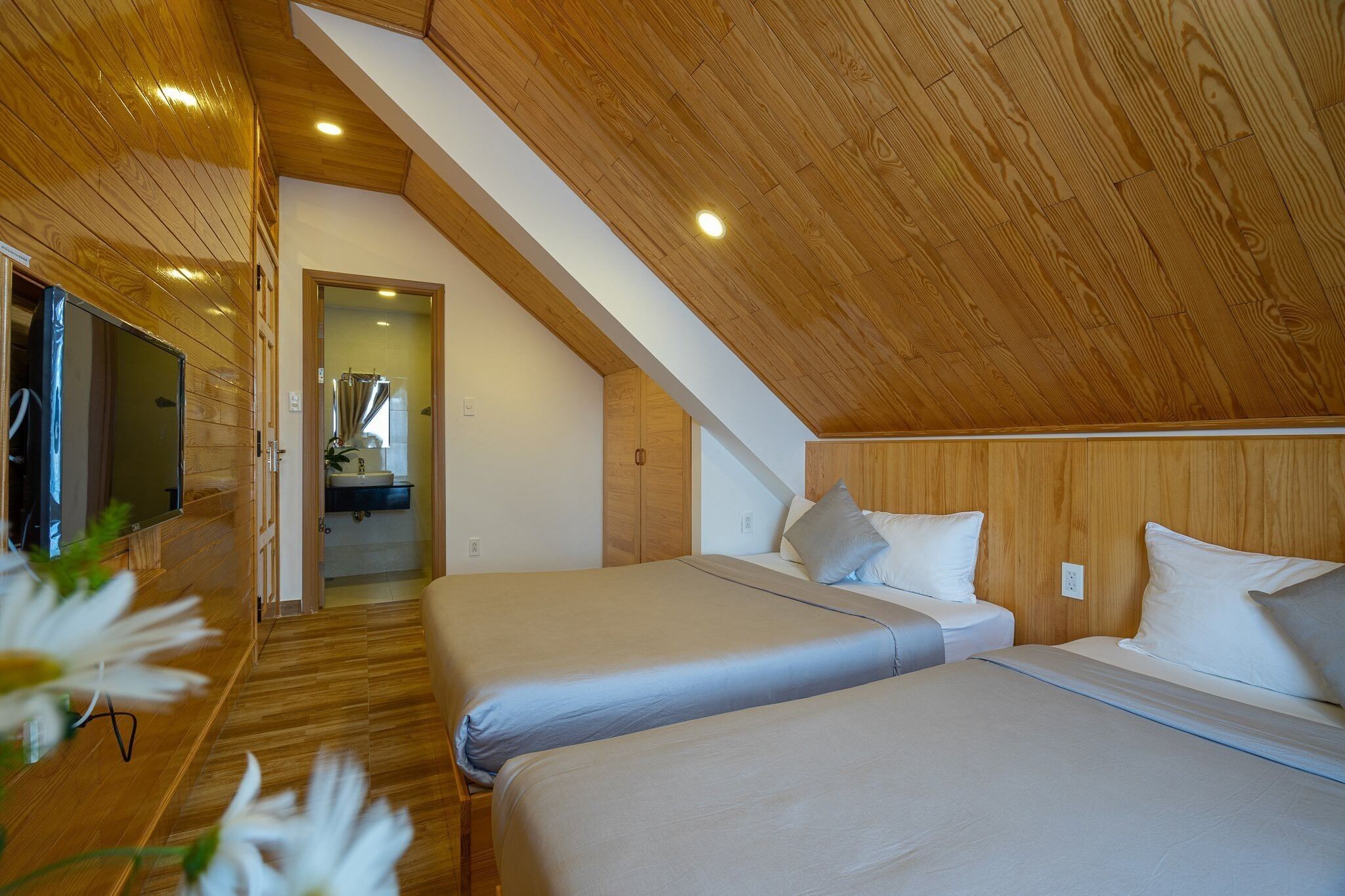 Quarto com duas camas, teto de madeira e banheiro à vista.