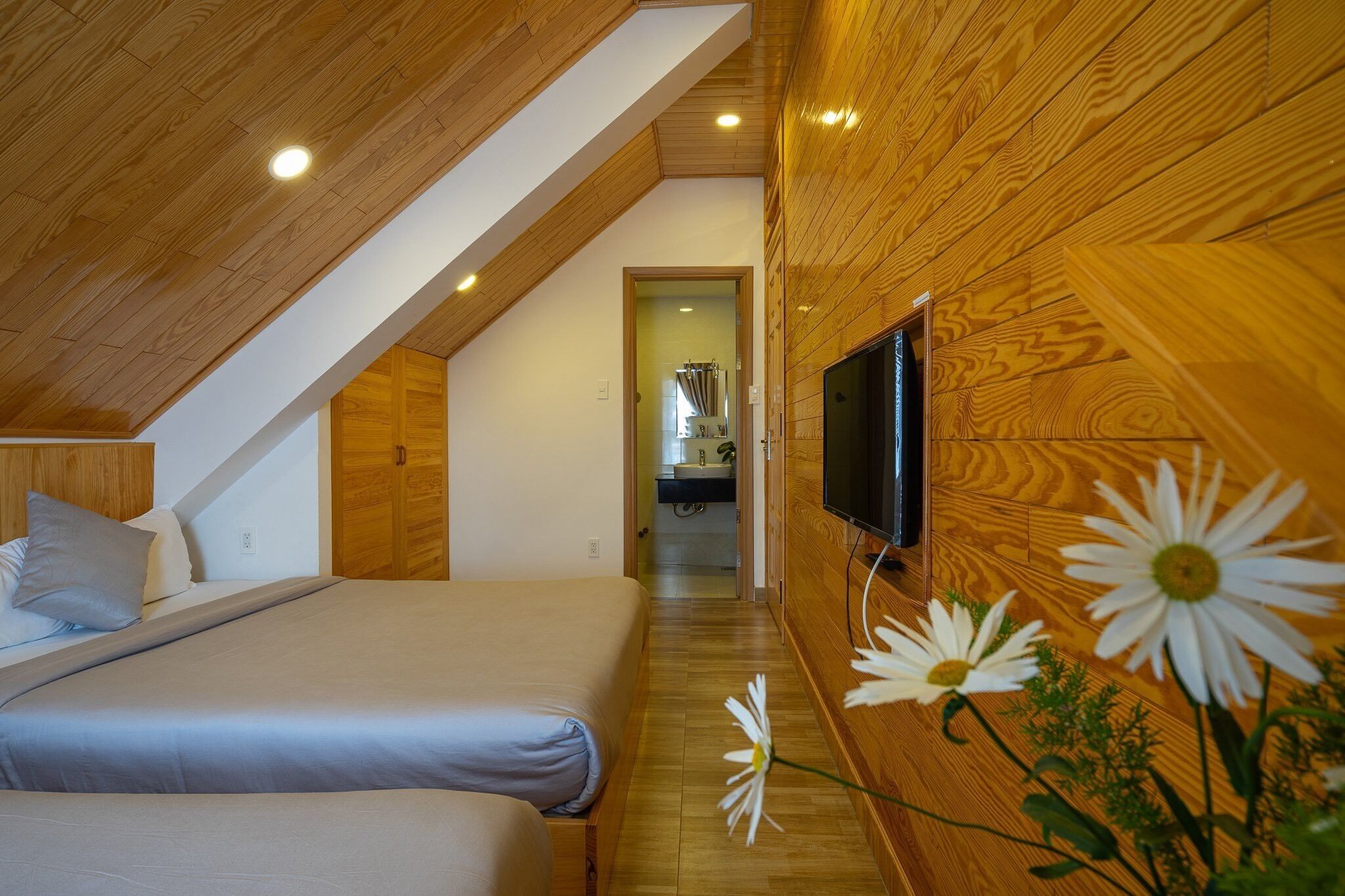 A bedroom with wooden paneling, a TV mounted on the wall, and a bed with pillows.
