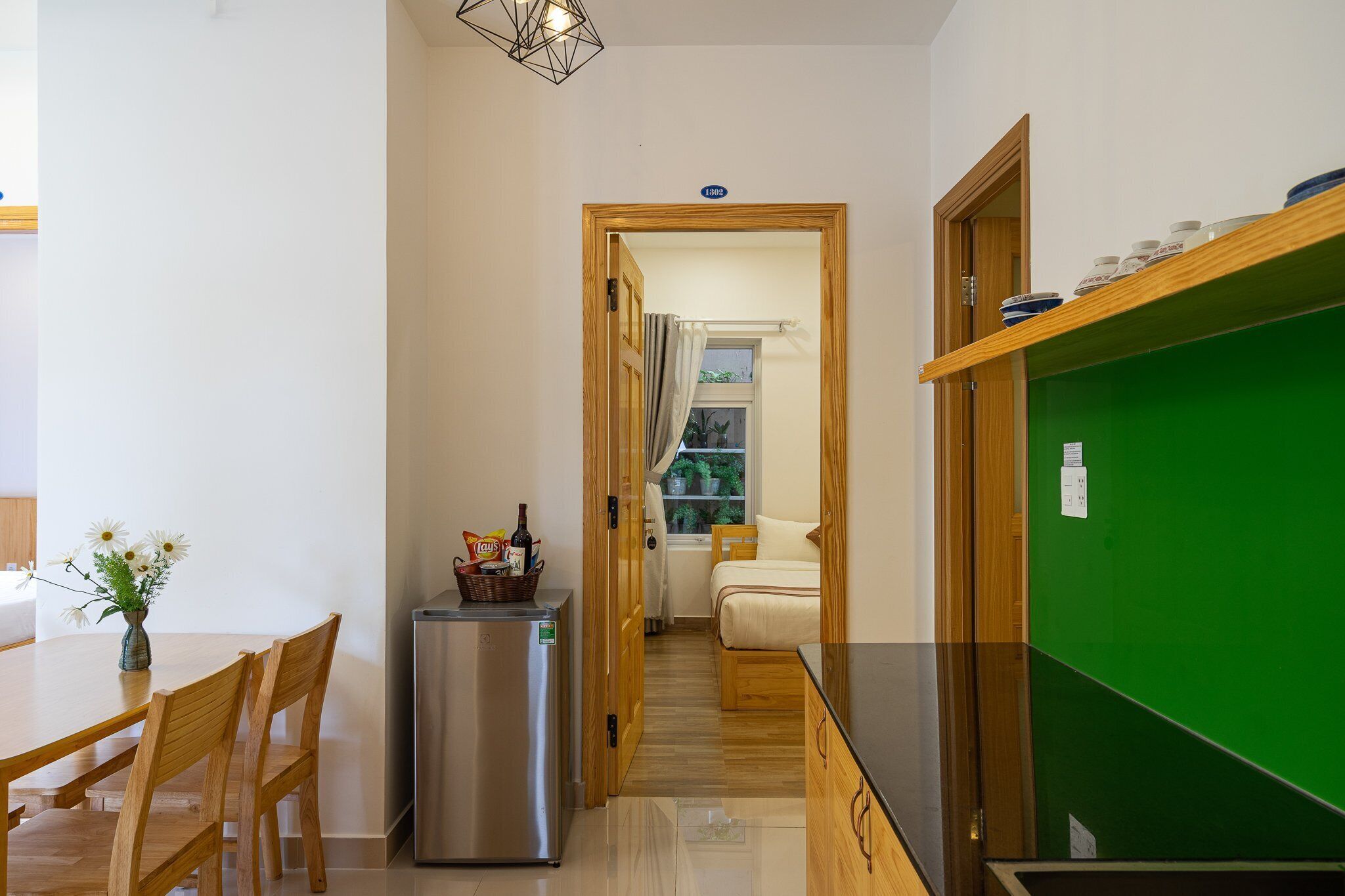 A compact room with a kitchenette, a dining area with wooden chairs, a small refrigerator, and a green accent wall.
