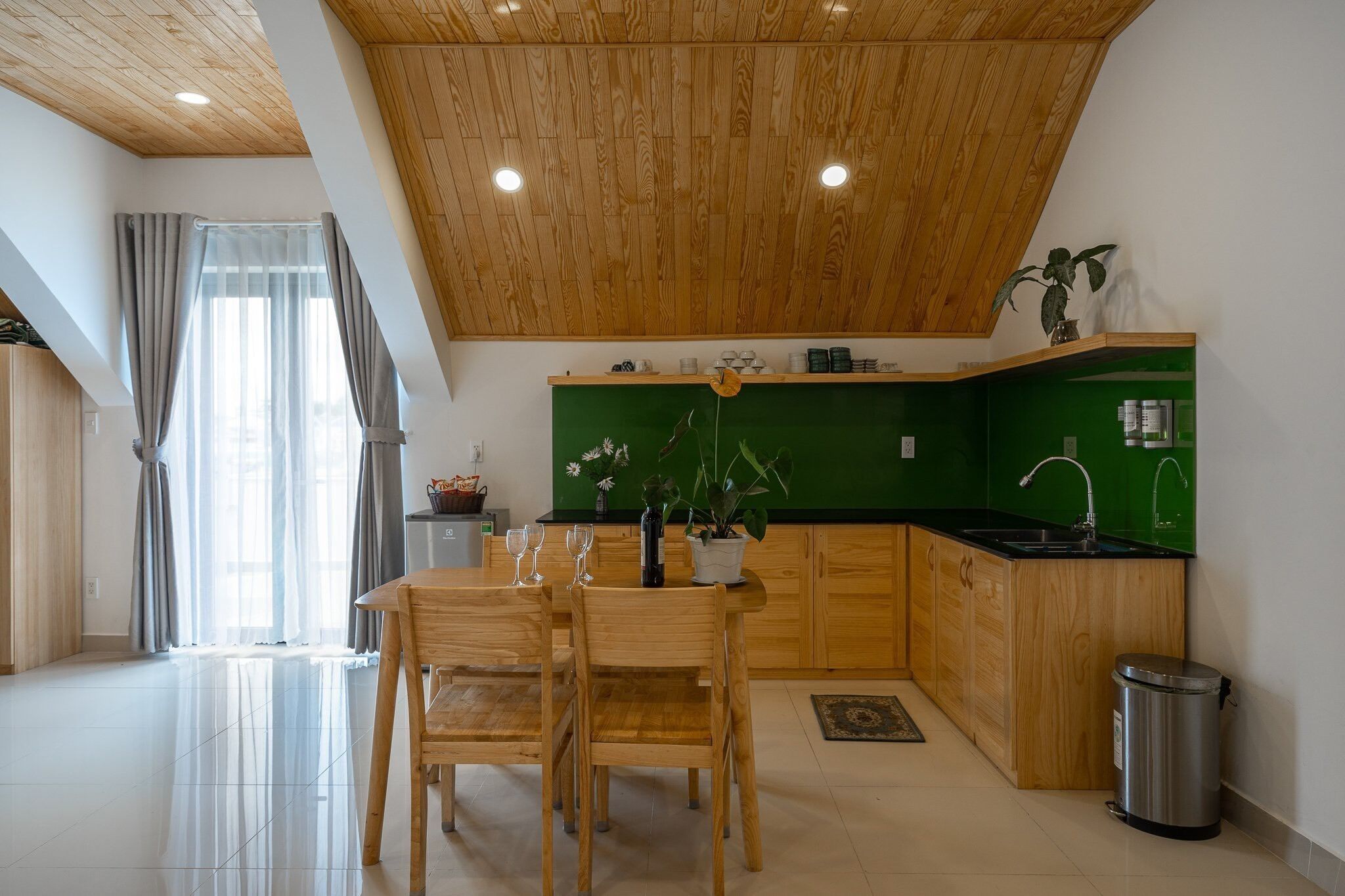 Een moderne keuken met houten kastjes, een groene spatwand en een eethoek met een houten tafel en stoelen.