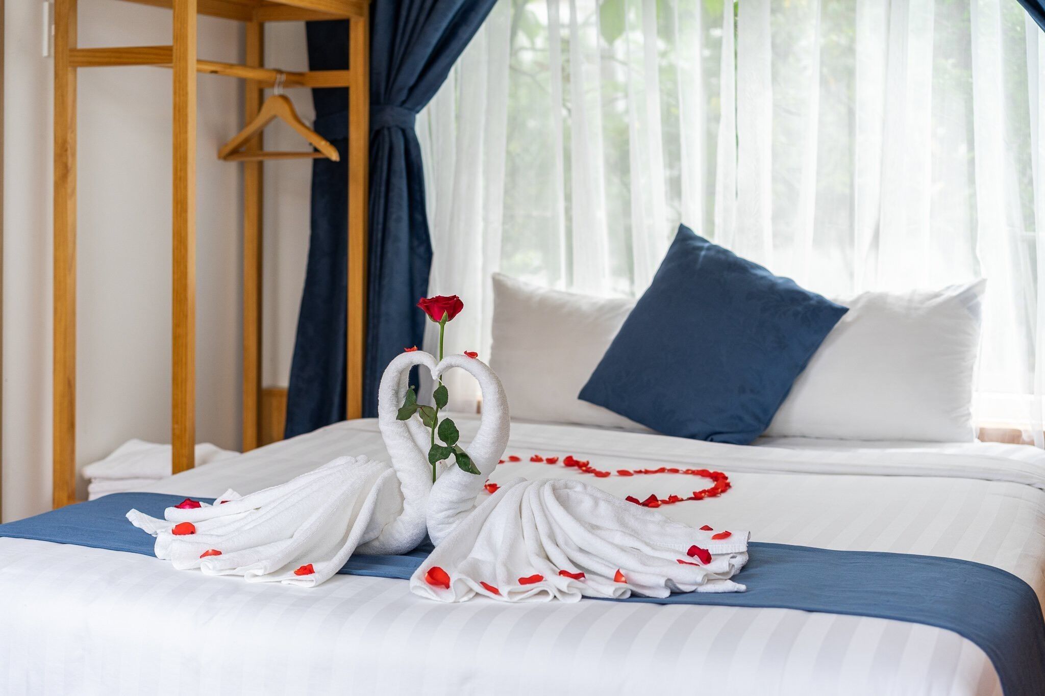 Una cama bien hecha con ropa de cama blanca y azul, una almohada azul y un perchero de madera a la izquierda.