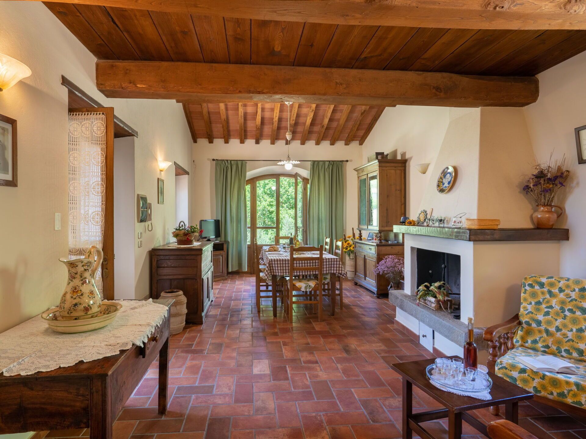 Un intérieur rustique avec un plafond en bois, un coin repas comprenant une table et des chaises, une cheminée et un canapé à motifs floraux.