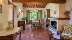 A rustic interior with a wooden ceiling, a dining area with a table and chairs, a fireplace, and a sofa with a floral pattern. - Wonderful private villa for 6 people with private pool, WIFI, TV, terrace and pets allowed (Castiglion Fiorentino)
