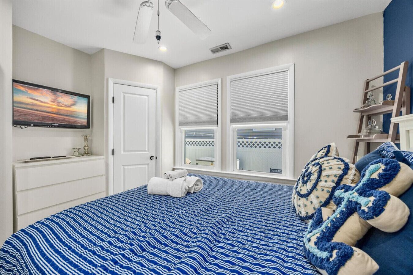 A bedroom with a bed, a TV, a window with blinds, and a ceiling fan.