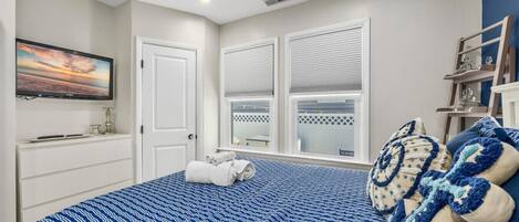 A bedroom with a bed, a TV, a window with blinds, and a ceiling fan.