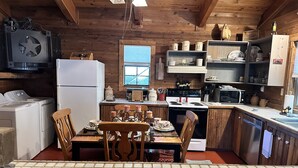 A cozy kitchen with wooden walls, a dining table, chairs, a refrigerator, a stove, and a microwave. - Beautiful Rustic Cabin 
Just 10 Minutes to Granbury square  (Granbury)