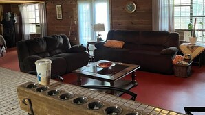 A cozy living room with a wooden ceiling, a fireplace, a sofa, a coffee table, and a large window with curtains. - Beautiful Rustic Cabin 
Just 10 Minutes to Granbury square  (Granbury)