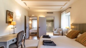 A hotel room with a bed, a desk, a chair, a bedside table, a lamp, and a painting on the wall.