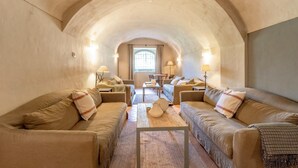 A cozy, arched room with two sofas facing a central table, a window with curtains, and a lamp on each side.