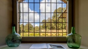 A window with a view of trees and a building, two empty green bottles, and an open book on a ledge.