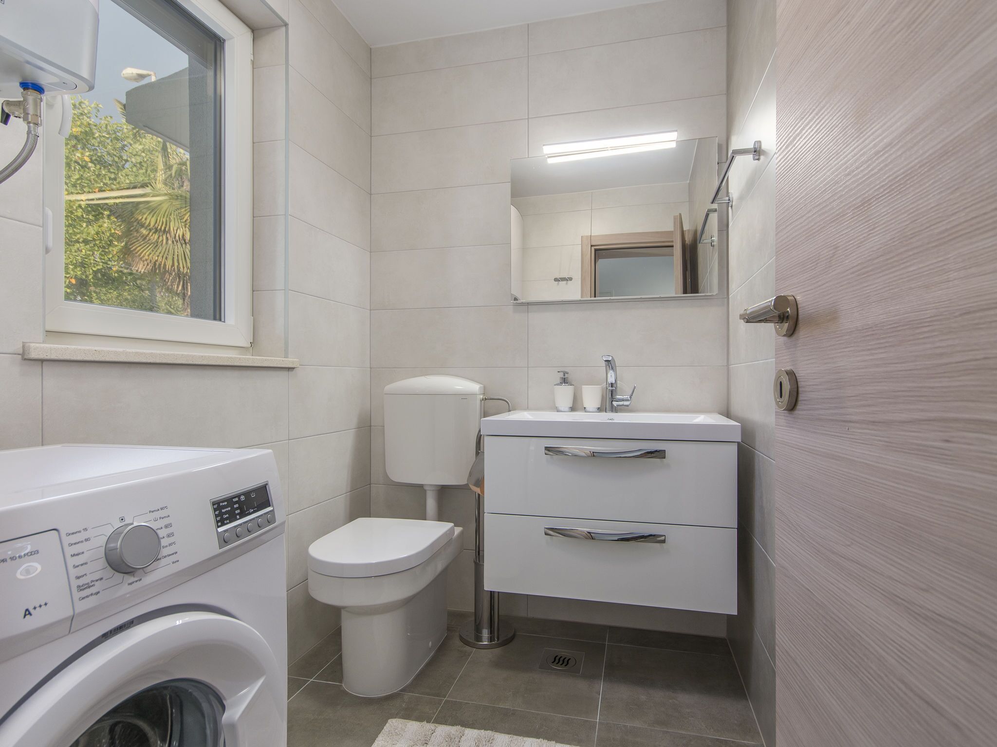 A compact bathroom with a washing machine, toilet, sink, and a mirror above the sink.