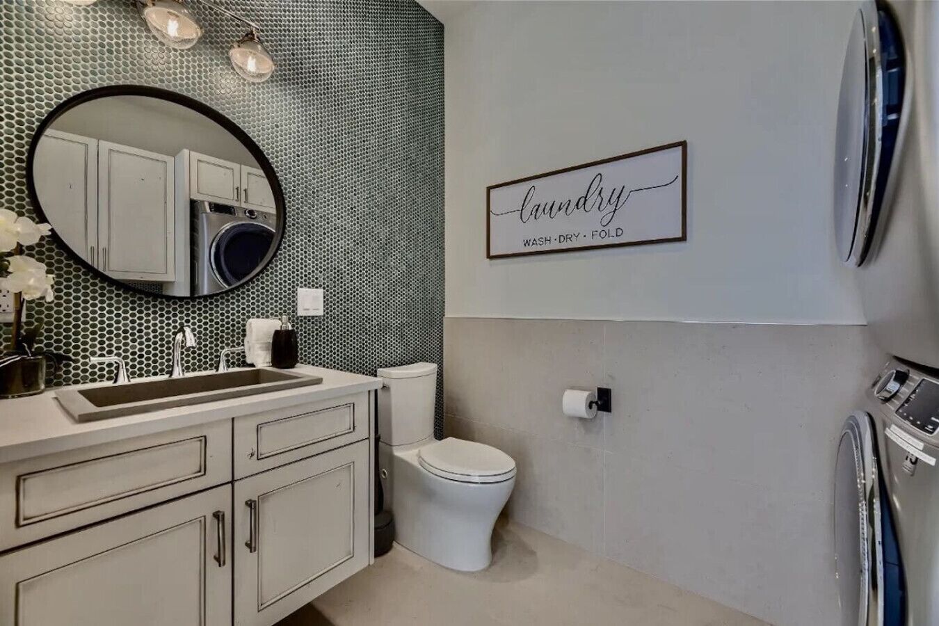 Un baño moderno con lavamanos, espejo, inodoro y un cartel en la pared que dice 'lavado, secado y doblado'.