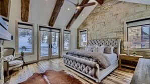 Une chambre avec un grand lit, des poutres en bois, des murs en pierre et une vue sur un paysage enneigé.