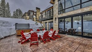 Une terrasse enneigée avec des sièges d’extérieur et un bâtiment en pierre doté de grandes fenêtres.