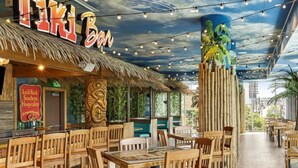 A restaurant with wooden furniture, a thatched roof, and a mural of a tropical scene.