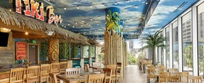 A restaurant with wooden furniture, a thatched roof, and a mural of a tropical scene.