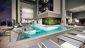 A modern indoor pool area with lounge chairs, a seating area, and a green wall feature.