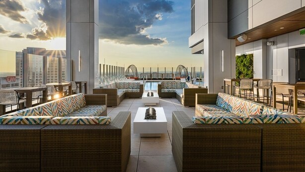 A rooftop lounge with wicker furniture, a pool, and a view of the city skyline.