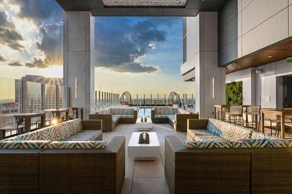 A rooftop lounge with wicker furniture, a pool, and a view of the city skyline.