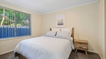 A bedroom with a bed, a nightstand, a window with blinds, and a picture on the wall.