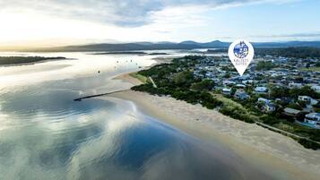 An aerial view of a coastal area with a beach, water body, and a cluster of houses.