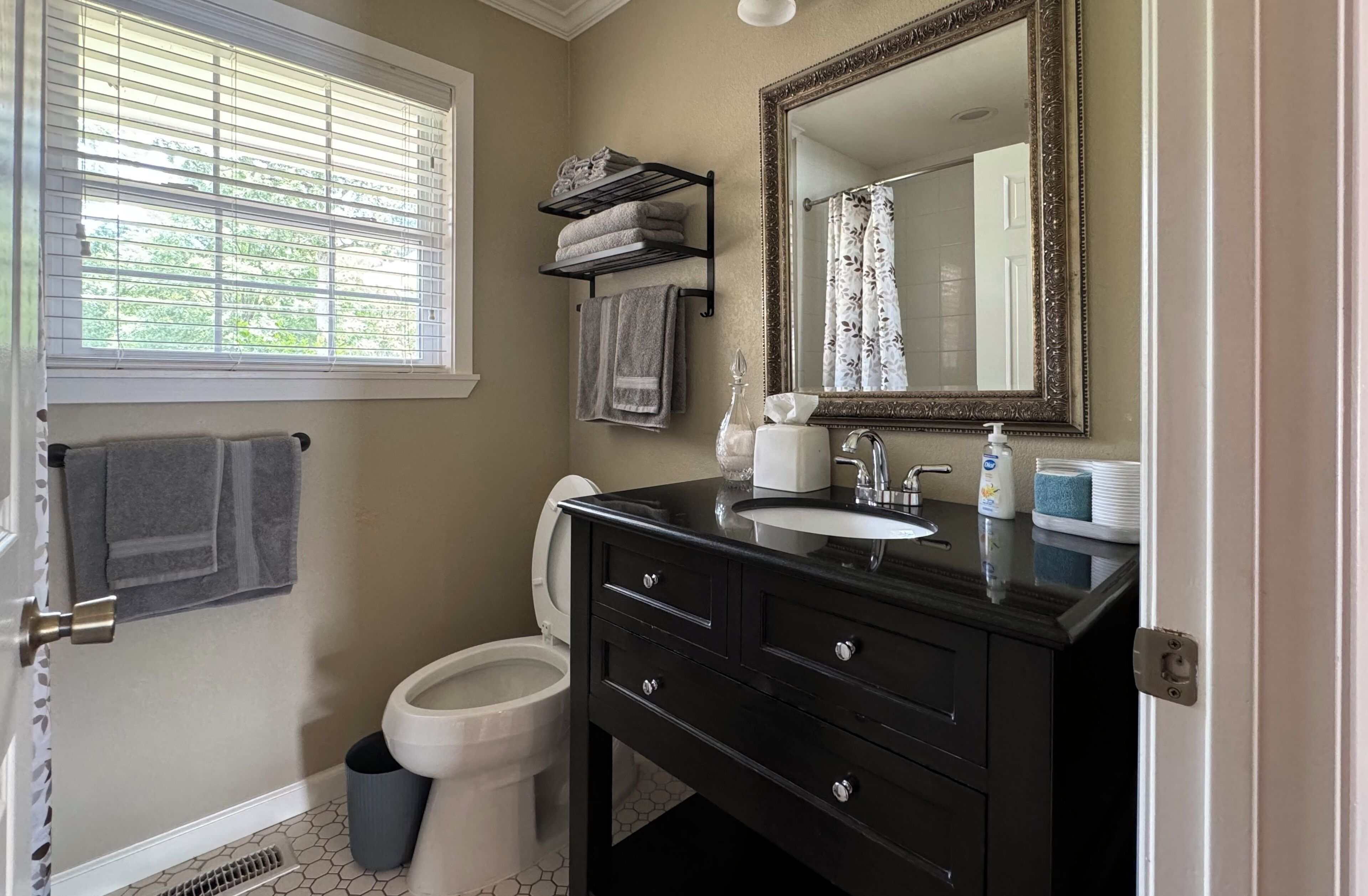 A bathroom with a black vanity, a white toilet, a towel rack, and a window with blinds.
