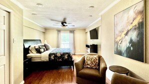 Ein Hotelzimmer mit Bett, Stuhl, Fernseher und Deckenventilator.