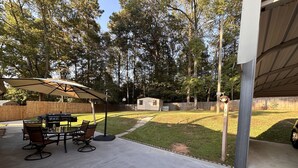 Eine Terrasse mit Grill und Essplatz, ein überdachter Sonnenschirm und ein Rasenstück mit Holzzaun.