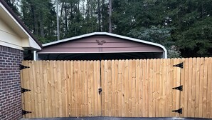 Eine Holztür zur Garage mit einem Metallriegel, eine Ziegelwand und ein Garagengebäude mit einem braunen Dach.