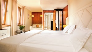 Quarto de hotel com uma cama grande, área de estar com sofá, uma mesinha com uma planta e banheiro com chuveiro de vidro.