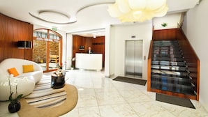 Um hall de hotel moderno com balcão de recepção, escada e área de estar com sofá e mesa de centro.