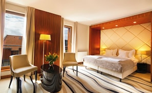 A hotel room with a large bed, two chairs, a round table with a vase, and a view of a building through the window. - Hotel Fahrenheit (Gdansk)