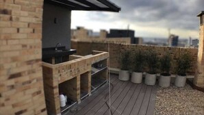 A rooftop patio with a brick barbecue area, potted plants, and a view of the city skyline. - Apartamentos Quinta Avenida (Bogotá)