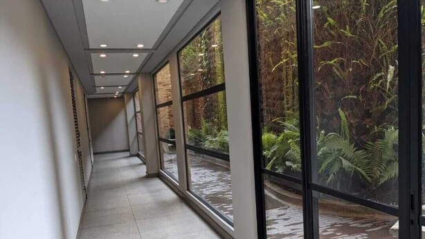 A corridor with large windows, a tiled floor, and a view of a garden. - Apartamentos Quinta Avenida (Bogotá)