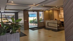 A hotel lobby with a reception desk, a large potted plant, and a view of the outside. - Apartamentos Quinta Avenida (Bogotá)