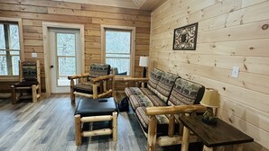 A cozy cabin interior with wooden walls and floors, a sofa, two chairs, a table, and a lamp. - Misty Mountain View @Smokies  #Xplorietickets:  Explore More, Experience More!! (Gatlinburg)